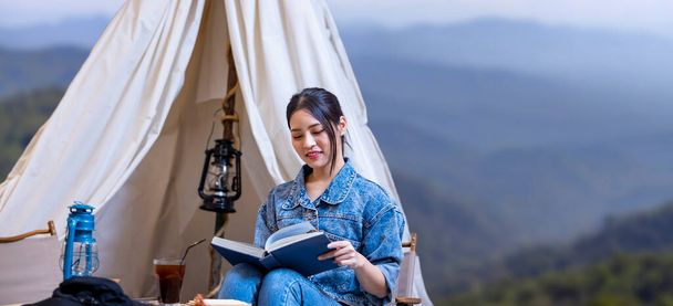 Азиатская женщина читает книгу во время одиночного похода лагерь на вершине горы с небольшой палаткой для занятий в выходные дни и наружной погони - Фото, изображение