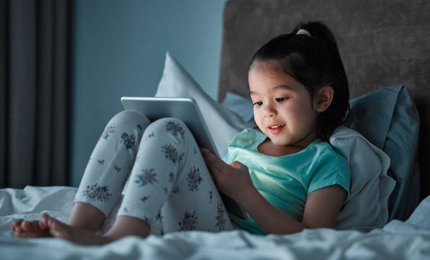 a little girl using a digital tablet while lying on her bed. - Φωτογραφία, εικόνα