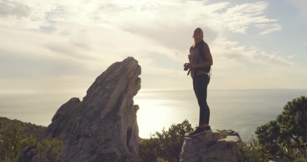 Jonge bergwandelaar bewonderende schilderachtige uitzicht vanaf piek langs groene heuvel trekking trail. Vrouw met verrekijker tijdens rotsachtige wandeling in afgelegen gebied met planten en struiken. Fit vrouw backpacken in de natuur. - Video