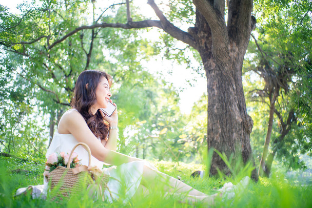 Iloinen nuori nainen puhuu älypuhelin kaupungin vihreä puisto aamu auringon valo - Valokuva, kuva