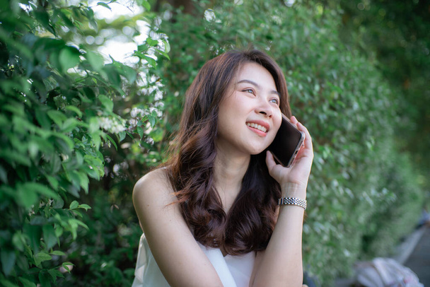 Веселая молодая женщина разговаривает смартфон в зеленом парке города утренний солнечный свет - Фото, изображение