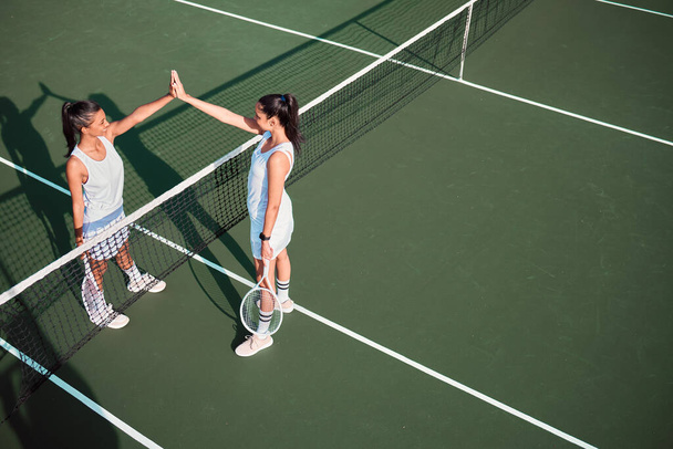 Две спортивные девушки дают друг другу пять, играя вместе в теннис на корте. - Фото, изображение