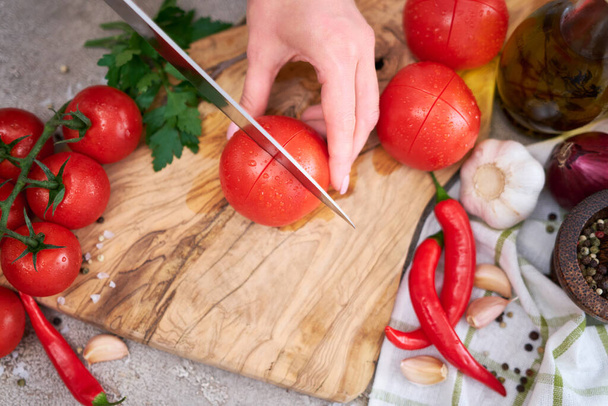 woman making notch on a tomato on wooden cutting board on grey kitchen concrete or stone table. - Fotoğraf, Görsel