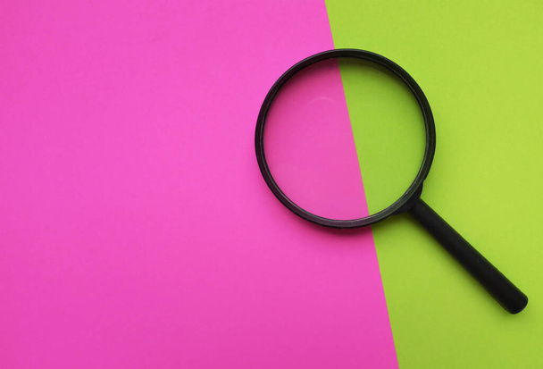 black round magnifying glass on pink and green background. used for searching or expanding books. - Foto, afbeelding