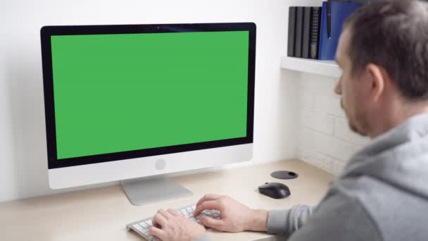 άνθρωπος που κάθεται στο χώρο εργασίας δακτυλογράφηση σε υπολογιστή πληκτρολόγιο με πράσινη οθόνη μινιμαλιστικό χώρο εργασίας στο σπίτι ή το γραφείο - Πλάνα, βίντεο