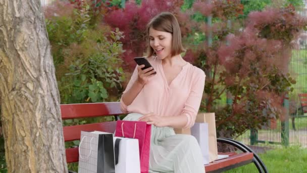 young woman taking photo her purchases in colored paper bags sharing in social media - Footage, Video