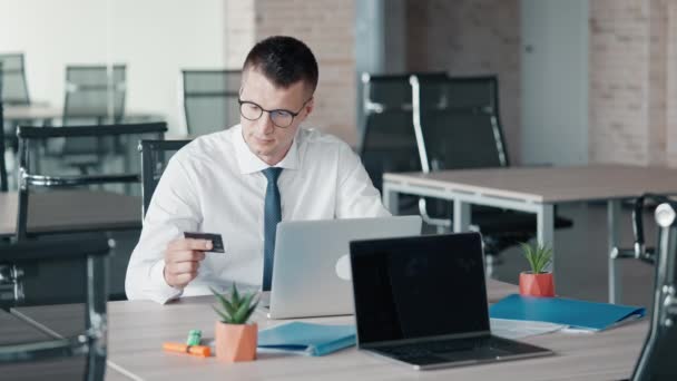hombre excitado gesto de la mano éxito hombre de negocios con camisa blanca y corbata celebración de la tarjeta de crédito con el ordenador portátil sentado en el lugar de trabajo en la oficina - Metraje, vídeo
