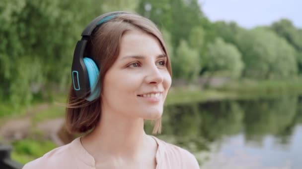 cerrar feliz mujer escuchando música auriculares caminando a lo largo de la orilla del río cámara lenta verano naturaleza al aire libre - Metraje, vídeo