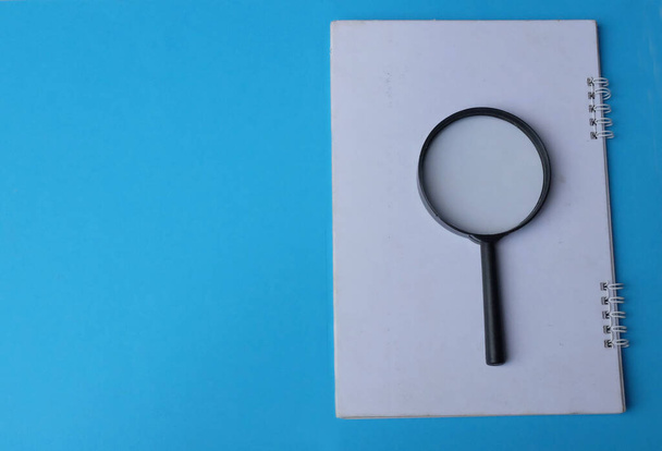 Lupe Suchsymbol auf Notizblöcken isolieren einen blauen Hintergrund - Foto, Bild