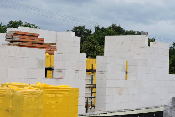 A house under construction, walls made of acc blocks, rough windows and door openings, reinforced brick lintels, a scaffolding, insulated foundation walls, solid concrete blocks and acc blocks on pallets - Fotó, kép