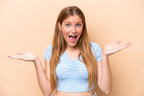 Young caucasian woman isolated on beige background with shocked facial expression - Фото, зображення