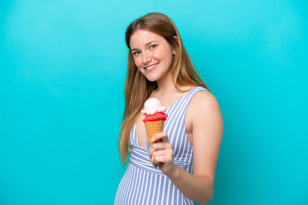 Young caucasian woman in swimsuit eating ice cream isolated on blue background with happy expression - Photo, Image