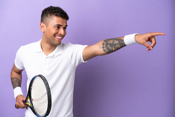 Young Brazilian man isolated on purple background playing tennis - 写真・画像