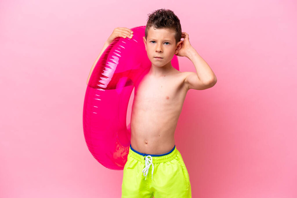 Little caucasian boy holding a inflatable donut isolated on pink background having doubts - Φωτογραφία, εικόνα