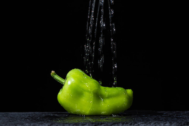 Νερό χύνεται σε πράσινο πιπέρι σε μαύρο φόντο. Φρέσκα και υγιεινά λαχανικά. Υγιεινή διατροφή - Φωτογραφία, εικόνα
