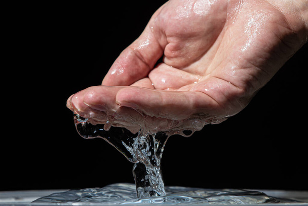 El agua vierte de la mano sobre la superficie del agua sobre un fondo negro. Agua potable limpia. - Foto, imagen