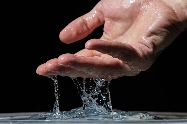 Water pours from the hand onto the surface of the water on a black background. Clean drinking water. - Foto, Imagem