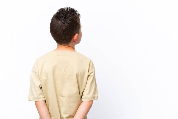 Pequeno menino caucasiano isolado no fundo branco na posição traseira e olhando para trás - Foto, Imagem