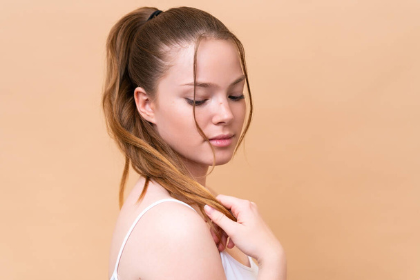 Mladá běloška izolovaná na béžovém pozadí dotýkající se jejích vlasů. Zavřít portrét - Fotografie, Obrázek