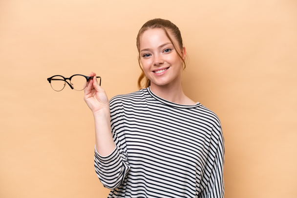 Young caucasian girl with glasses isolated on beige background smiling a lot - Photo, Image