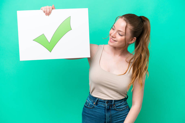 Young caucasian woman isolated on green background holding a placard with text Green check mark icon with happy expression - Photo, Image