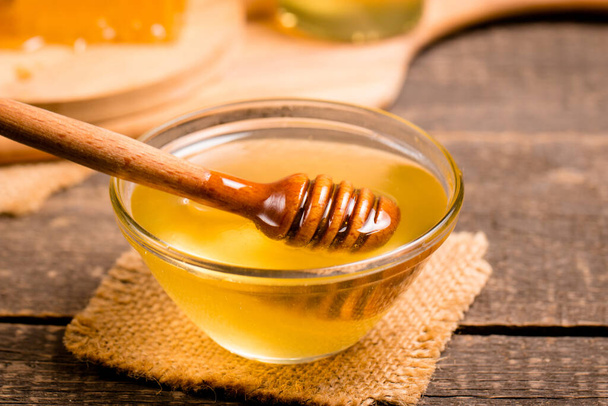 Honey dripping from a honey dipper on wooden rustic background - Φωτογραφία, εικόνα