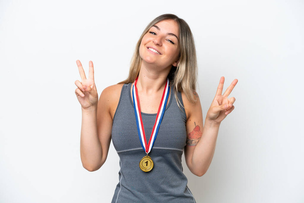 Молодая румынская женщина с медалями на белом фоне показывает знак победы обеими руками - Фото, изображение