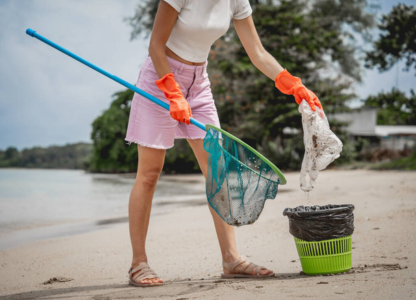 A female ecologist volunteer cleans the beach on the seashore from plastic and other waste. - Photo, Image