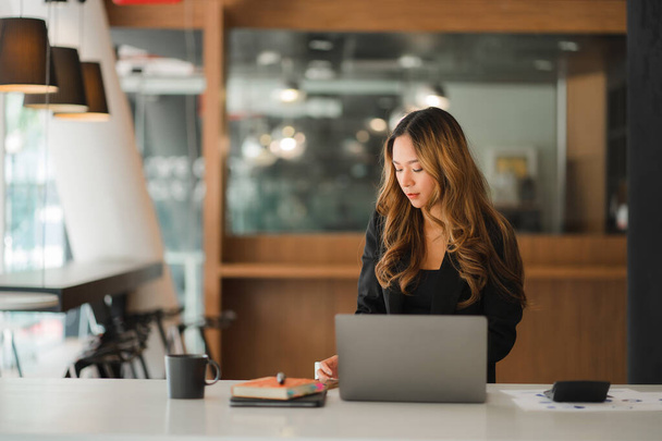 Внештатная молодая азиатская бизнесвумен, работающая на ноутбуке в современном офисе. составление отчета по анализу инвестиций в недвижимость Бухгалтерские концепции, финансовые системы и налоги. - Фото, изображение