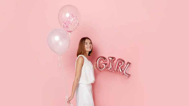 Beautiful young woman, dressed in a white, holdings a balloons, over pink background. - Fotó, kép