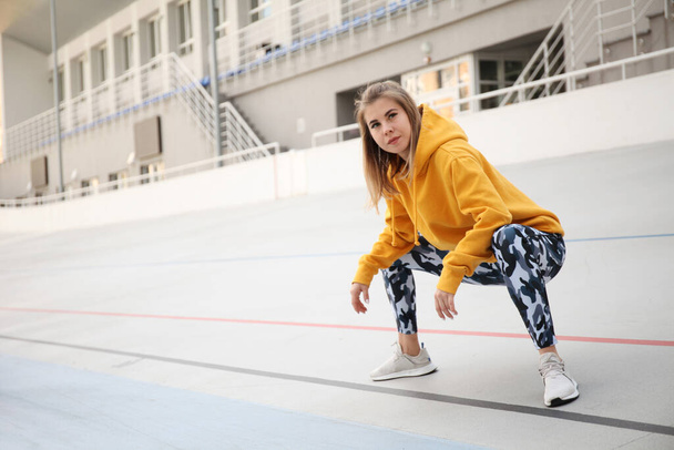 Pretty woman in yellow top and military leggings does warm-up before outdoor sports. - 写真・画像