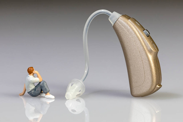 miniature figure beneath gold colored hearing aid - 写真・画像