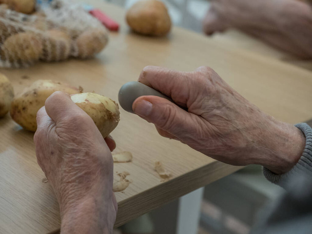 Old, hands are peeling potatoes - Foto, Imagen