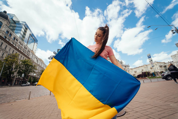 Young woman with national flag of Ukraine walking in the city - Foto, imagen