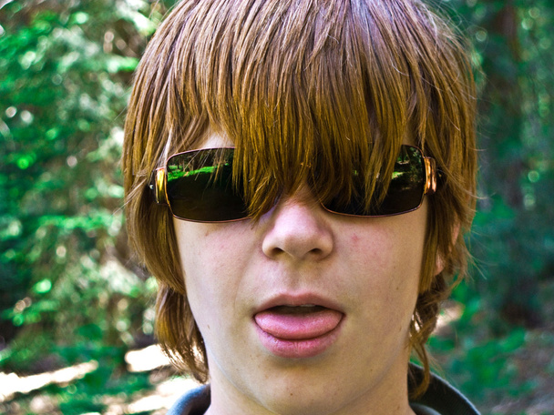 Мальчик с рыжими длинными волосами и солнцезащитными очками впивается в язык и выглядит настоящим.
 - Фото, изображение