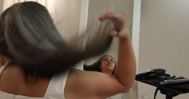 Kobieta kontrolująca prostowanie swoich szaro-czarnych włosów, które sama zrobiła, czesając je szczotką, podając dłonie i palce nad włosami, odbite w lustrze, białe tło - Materiał filmowy, wideo