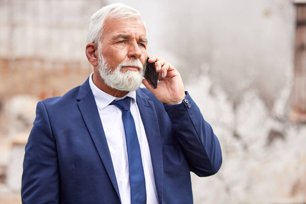 un uomo d'affari anziano che utilizza uno smartphone su uno sfondo urbano. - Foto, immagini