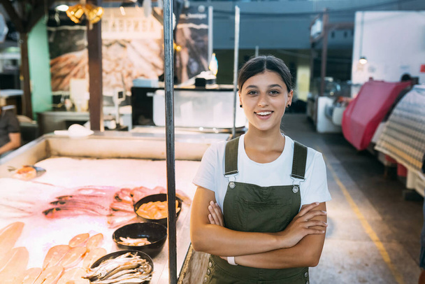 Smiling female fishmonger standing near seafood shop counter - 写真・画像