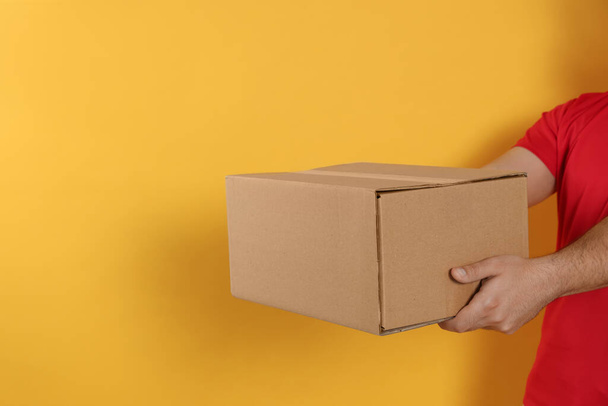 Courier holding cardboard box on yellow background, closeup. Space for text - Fotoğraf, Görsel