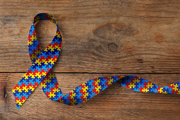 World Autism Awareness Day. Colorful puzzle ribbon on wooden background, top view - Foto, afbeelding