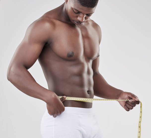 a man measuring his waist using a measuring tape against a studio background. - Fotó, kép