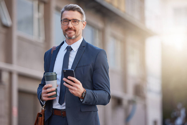 un hombre de negocios maduro bebiendo un café mientras usa un teléfono en la ciudad. - Foto, Imagen