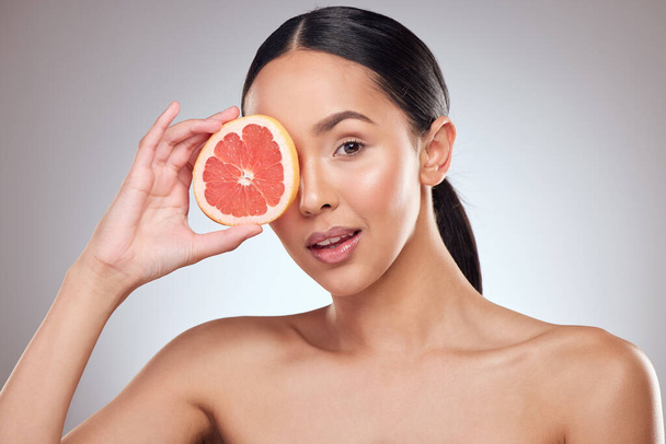 Studio portret van een mooie jonge vrouw poseren met grapefruit tegen een grijze achtergrond. - Foto, afbeelding