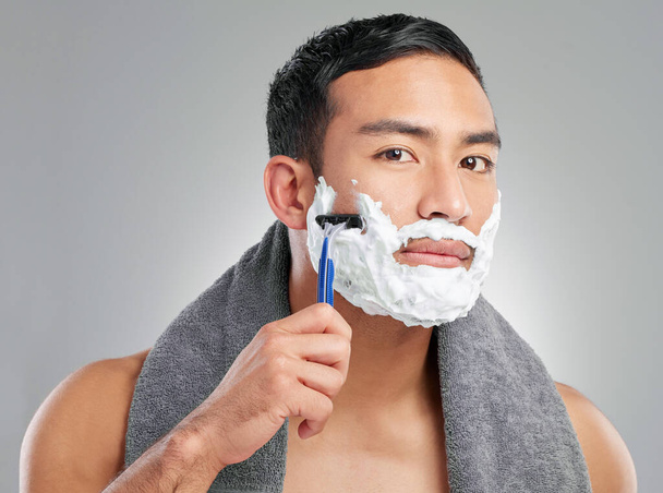 Studio shot of a handsome young man shaving against a grey background. - 写真・画像