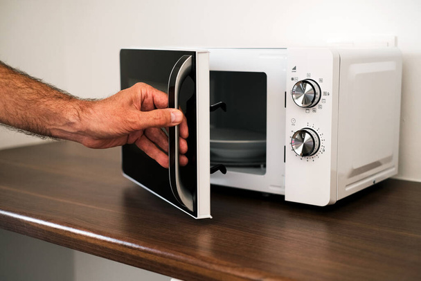 a man puts a plate in the microwave to warm up his food - Photo, Image