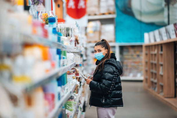 Молодая женщина в маске покупает в супермаркете - Фото, изображение
