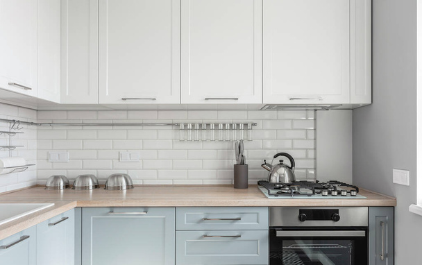 Σχεδιασμός μοντέρνας ελαφριάς λευκής κουζίνας με μπλε ντουλάπια κουζίνας και φωτιστικά πατώματος. Υψηλής ποιότητας φωτογραφία - Φωτογραφία, εικόνα