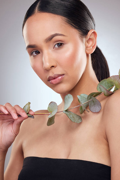 Studio portrait of a beautiful young woman posing with eucalyptus against a grey background. - Фото, зображення