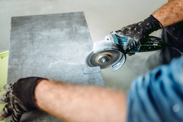 professional caucasian construction worker cutting ceramic tiles with angle grinder during tiling works - Fotografie, Obrázek