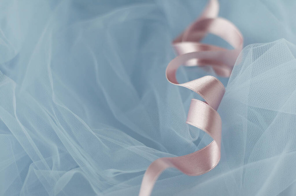 Light-pink silk satin ribbon curled in spirals on light-blue background. Wrapping decoration on tulle fabric. Packaging process  - Φωτογραφία, εικόνα